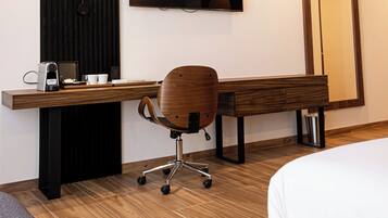 A modern hotel room with a wooden desk, a chair, a bed, a flat-screen TV, and a large mirror.
