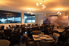 A restaurant with multiple tables and chairs, large windows, and a modern chandelier. - Radisson San Luis Potosi Aeropuerto (San Luis Potosi)