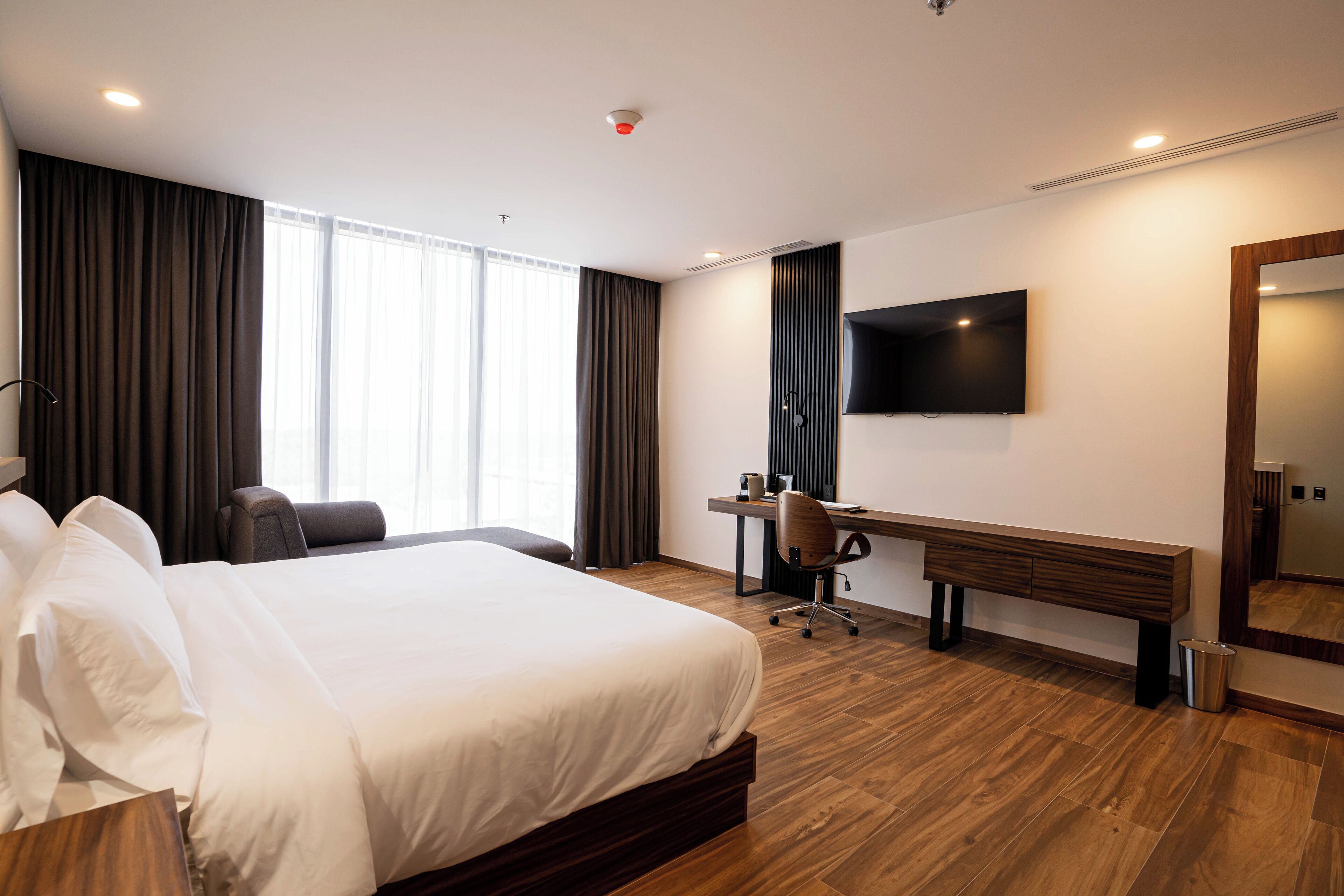 A hotel room with a large bed, a desk, a chair, a TV, and a mirror.