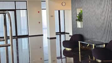 Un vestíbulo moderno con piso negro reflectante, una recepción y un área de descanso con sillas.