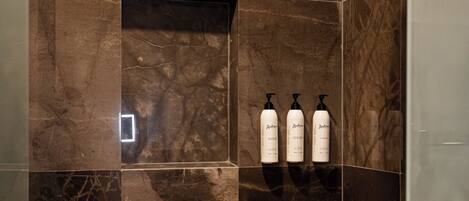 Un baño moderno con baldosas de mármol oscuro, un cabezal de ducha y tres botellas de champú.