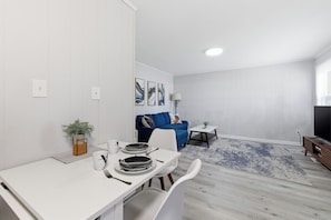 A modern living room with a dining area, a blue sofa, a TV, and a lamp.
