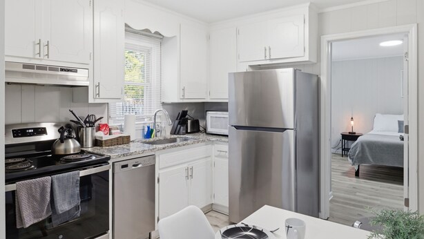 A modern kitchen with white cabinets, stainless steel appliances, and a dining area with a table and chairs.