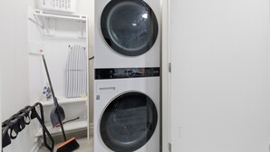 A laundry room with two stacked washing machines, a drying rack, and a broom.