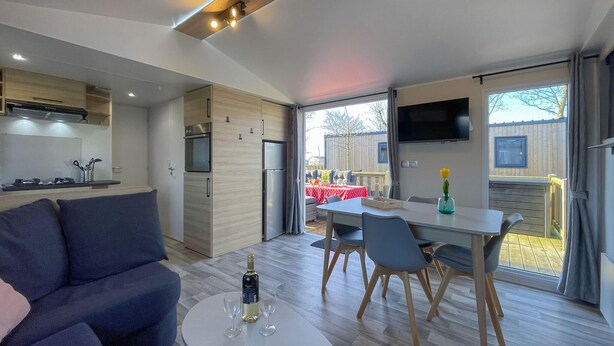 Een moderne woonkamer met een bank, een eettafel met stoelen, en een keuken met een koelkast en fornuis.