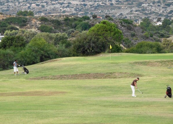 A golf course with a flag, a golfer preparing to hit a ball, and a golf bag.