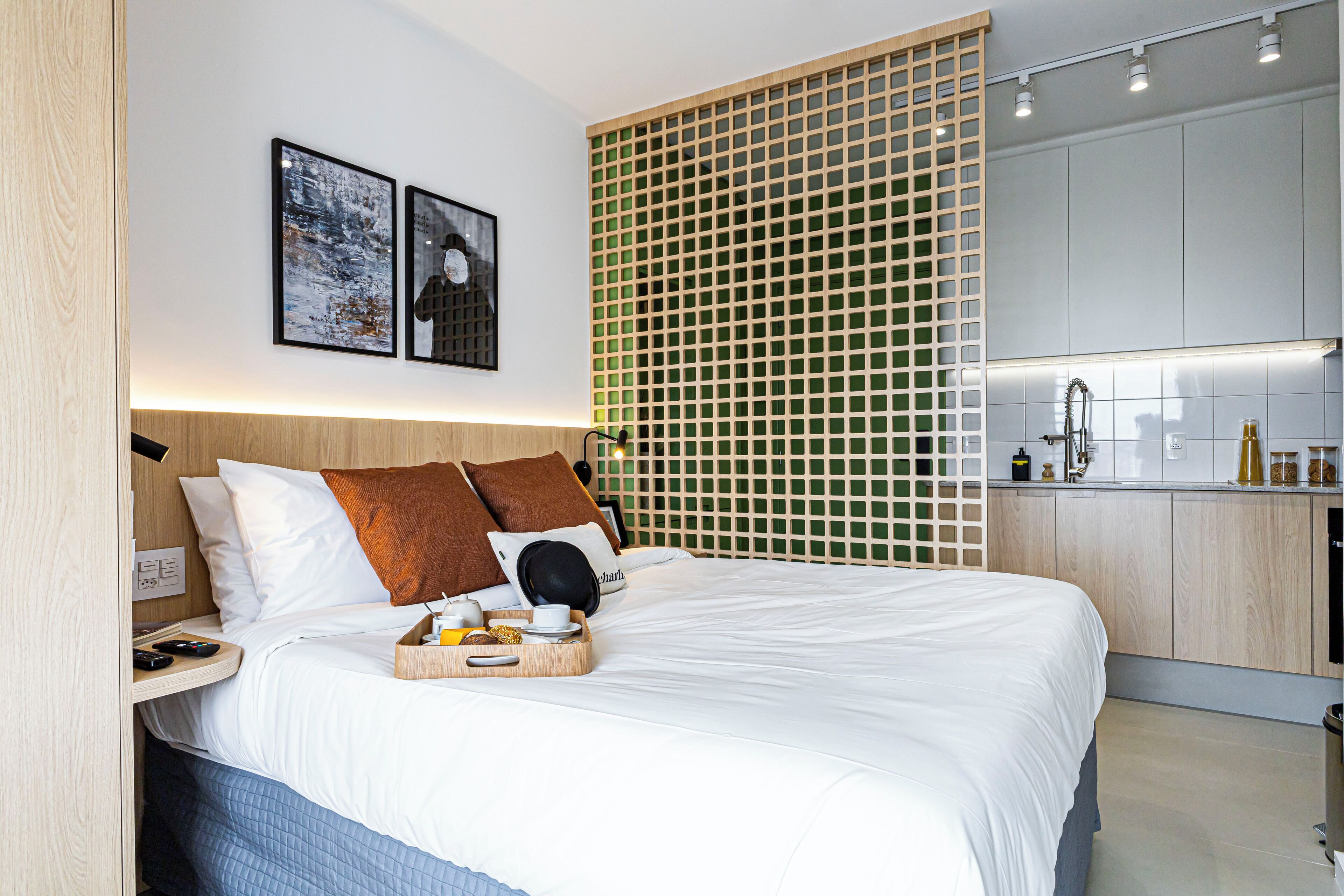 A modern hotel room with a large bed, a bedside table, a tray with breakfast items, and a view of the kitchen area.