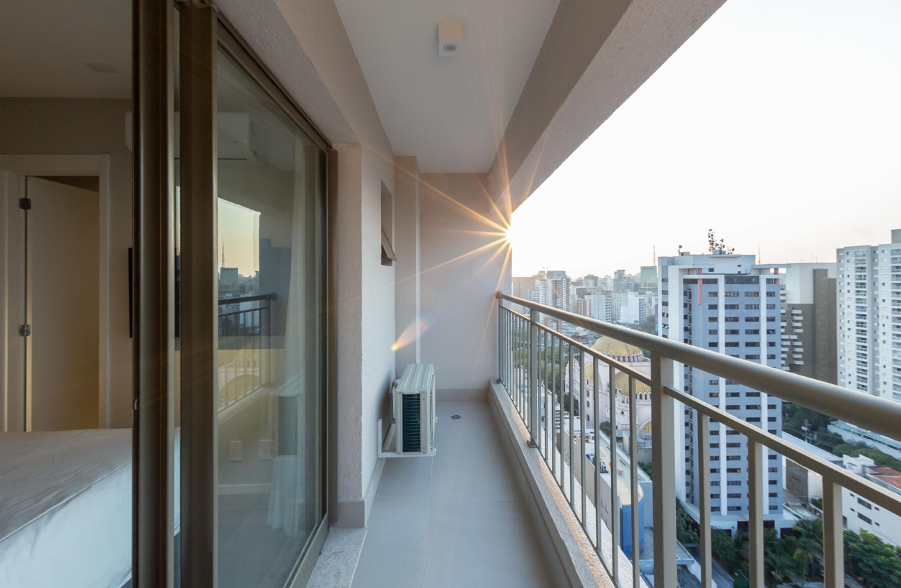 A balcony with a glass door, a small air conditioning unit, and a view of the cityscape.