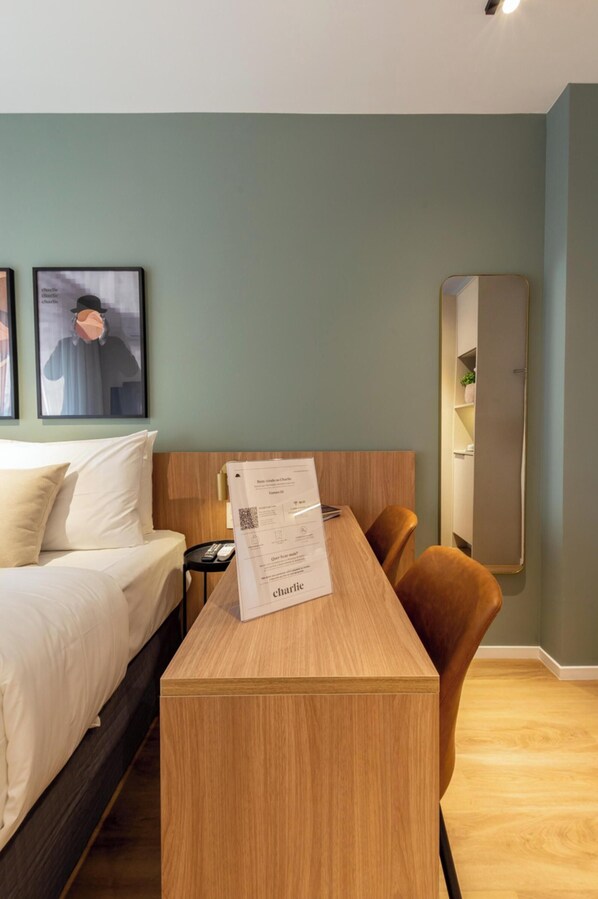 Ein Hotelzimmer mit einem Bett, einem Holztisch, einem Stuhl, einem Spiegel und zwei gerahmten Bildern an der Wand.
