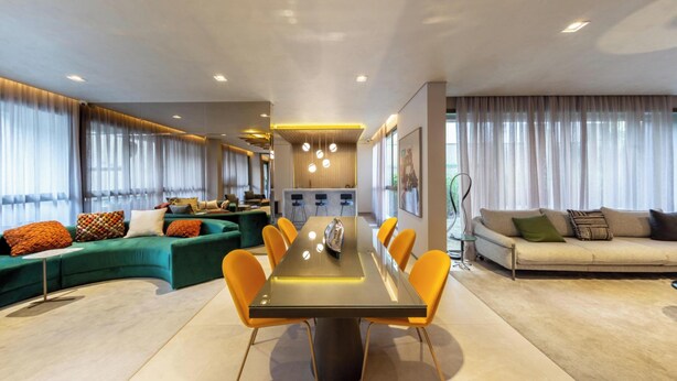 A modern living room with a dining area, green sofa, orange chairs, and a beige sofa.