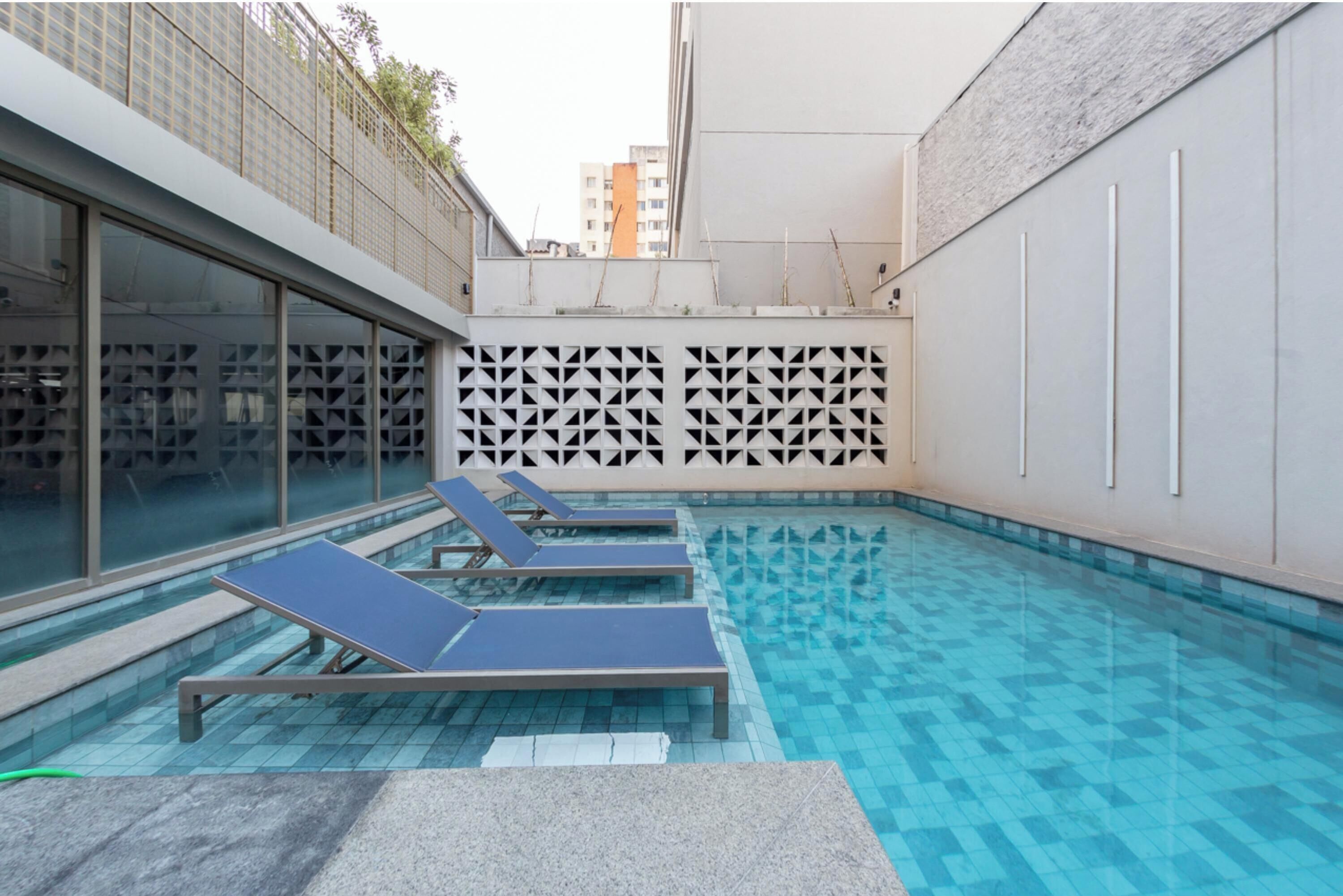 Une piscine dotée de chaises longues, d’un sol carrelé et d’un mur orné d’un motif géométrique.