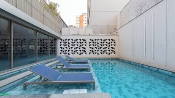 Une piscine dotée de chaises longues, d’un sol carrelé et d’un mur orné d’un motif géométrique.