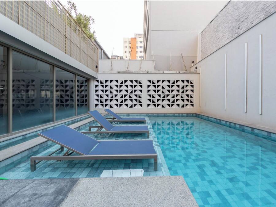 Une piscine dotée de chaises longues, d’un sol carrelé et d’un mur orné d’un motif géométrique.