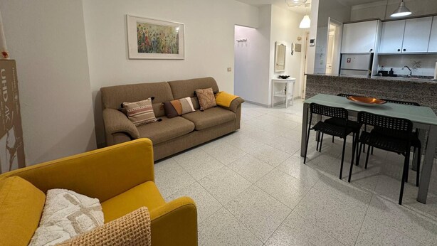 Un salon comprenant un canapé, un fauteuil jaune et un coin repas avec une table et des chaises.