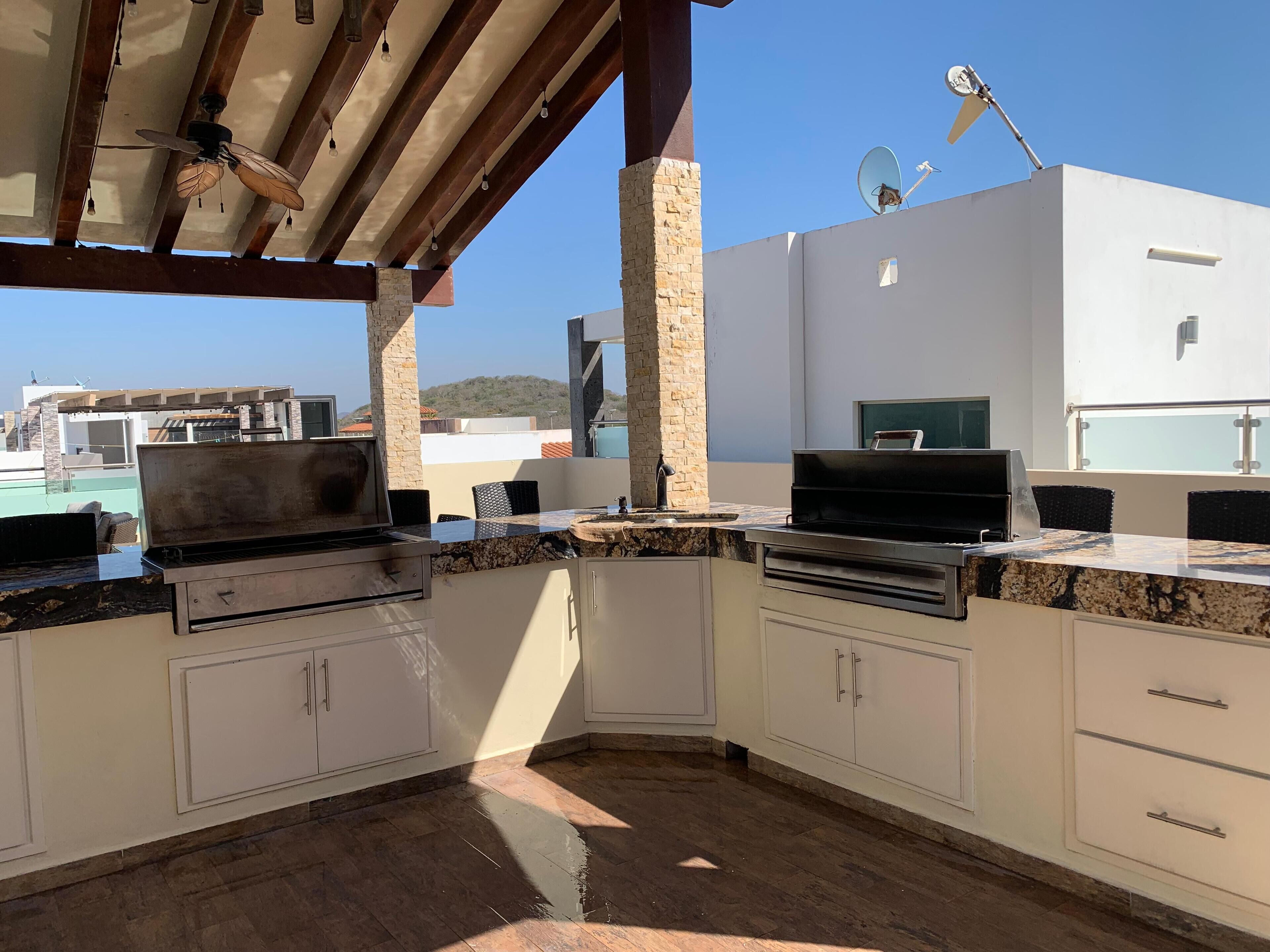 A covered outdoor kitchen with a grill, a sink, and a dining area.