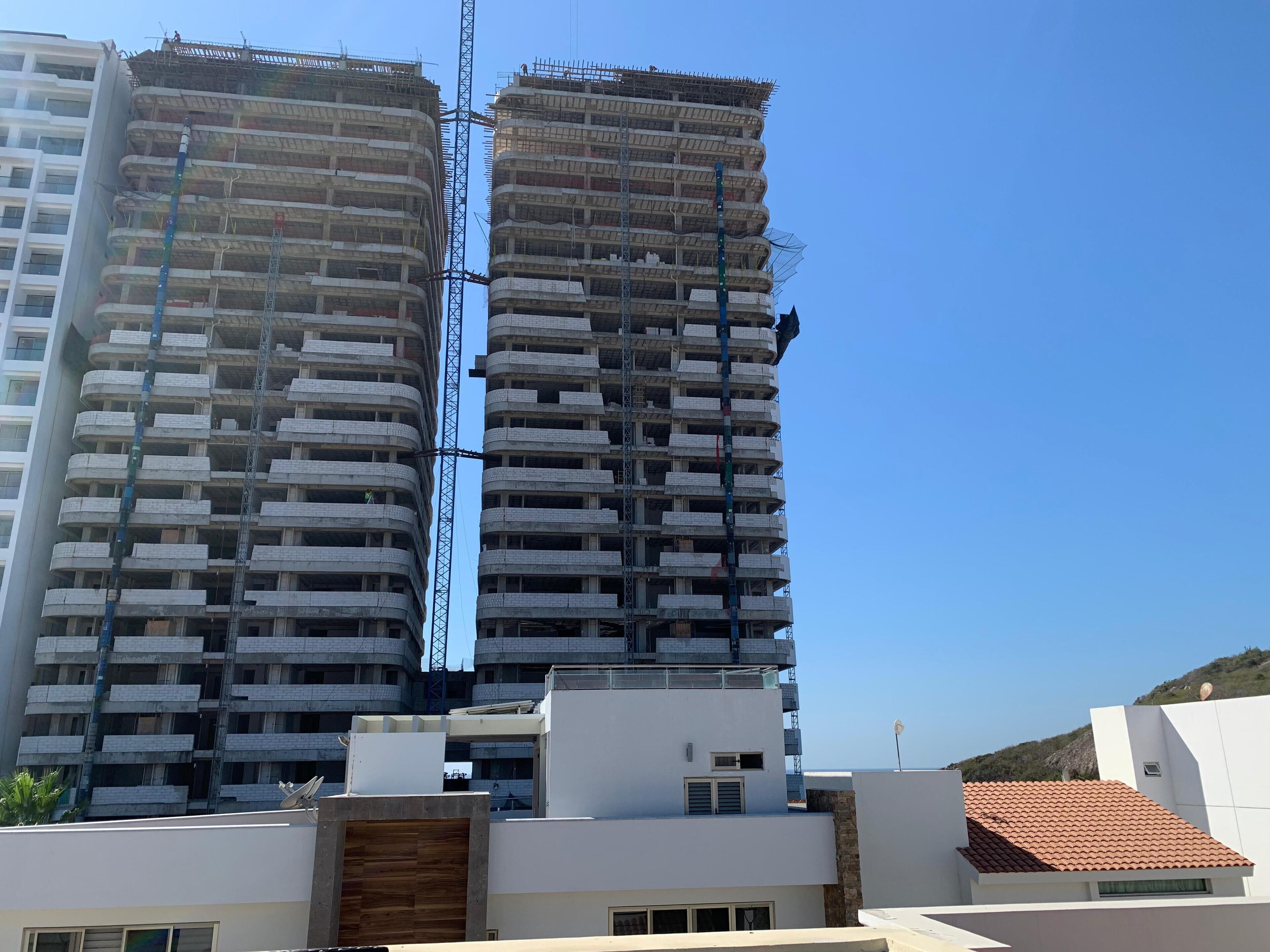 Two high-rise buildings under construction with visible scaffolding and construction workers.