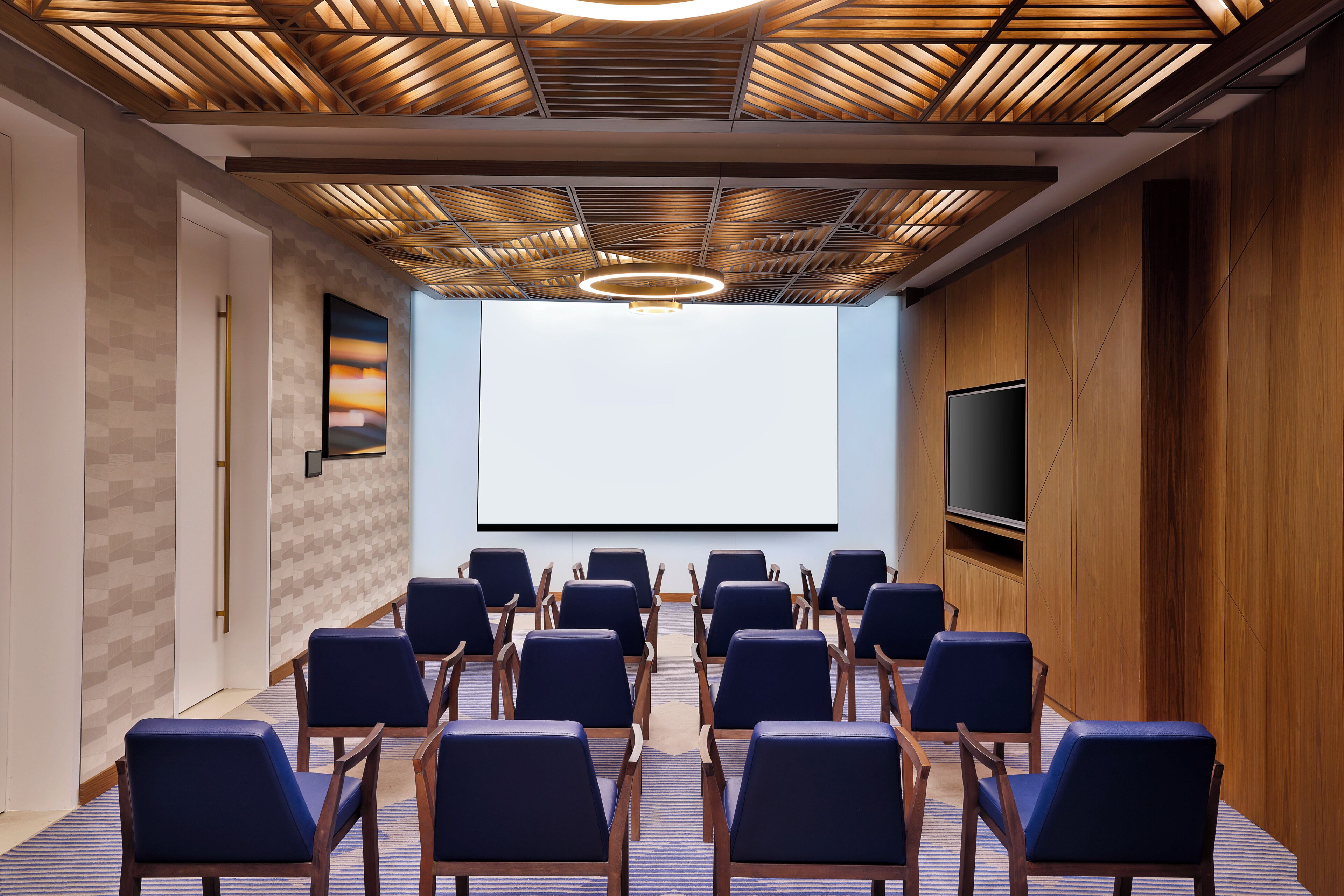 A conference room with a large screen, rows of chairs, and a wooden ceiling design.