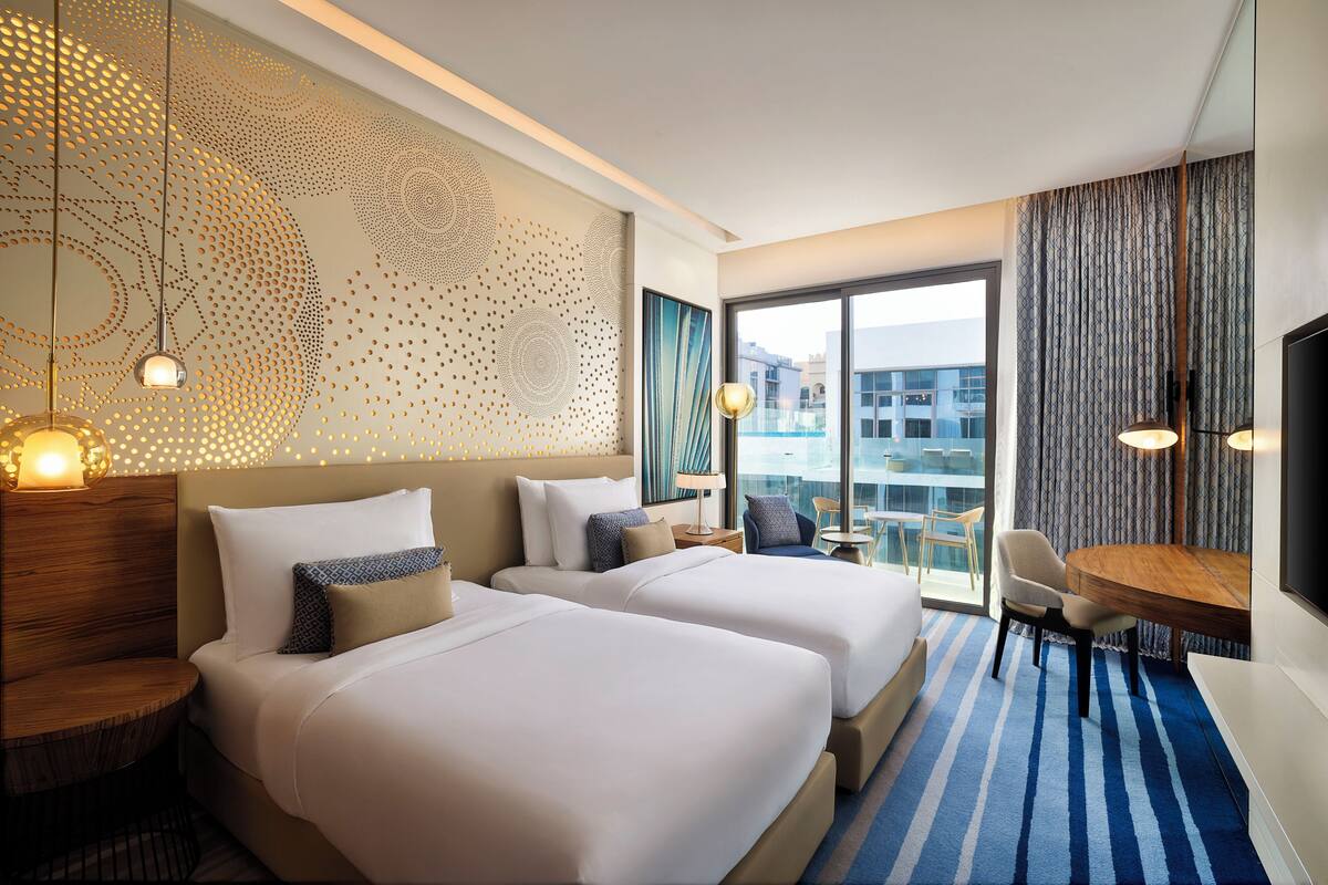 A hotel room with two beds, a dining table, and a large window with a view.