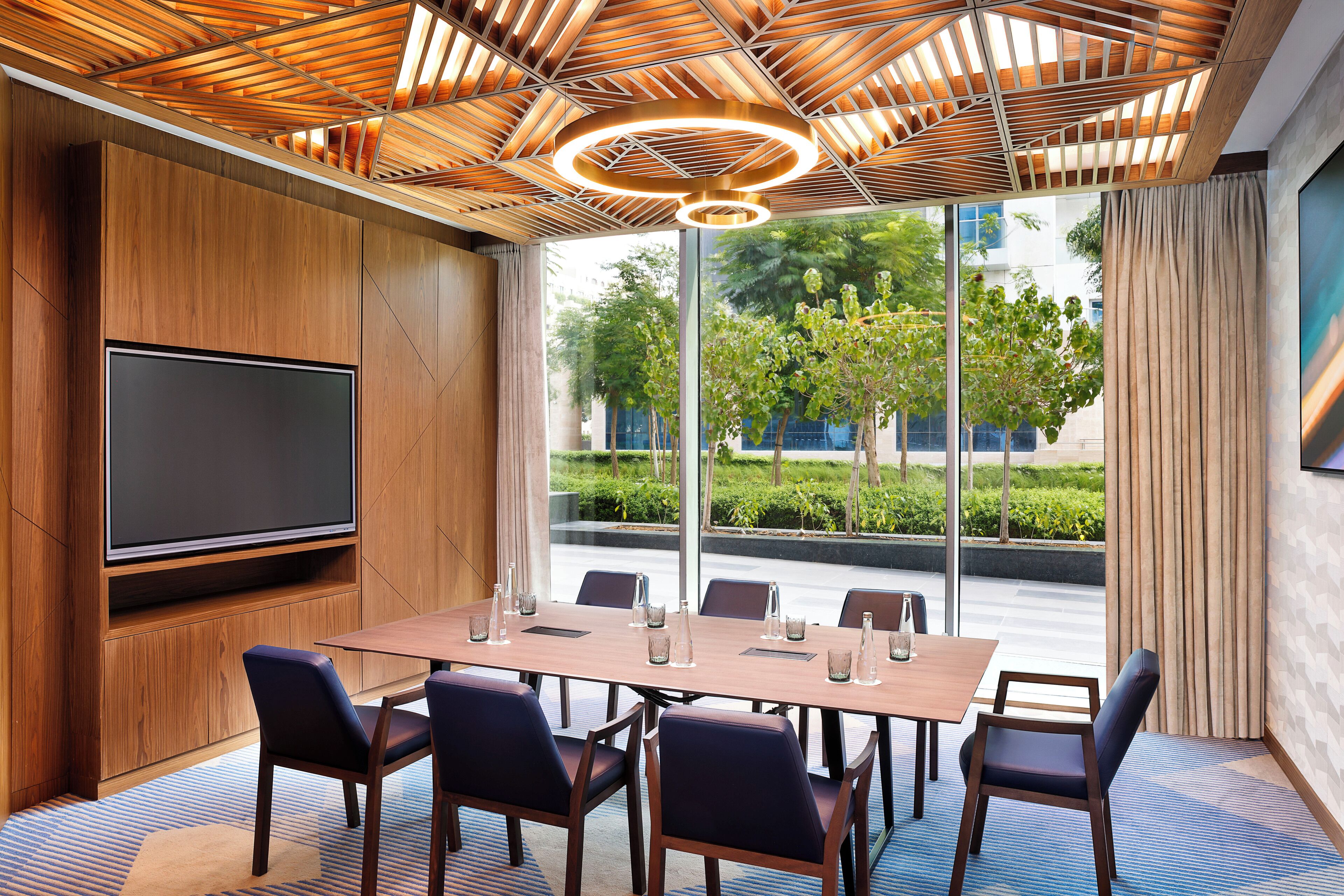 A conference room with a large flat-screen TV, a wooden ceiling, and a view of greenery outside.