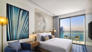 A modern hotel room with a large bed, a seating area, a view of the water, and a decorative wall. - Tumbi Hotel Dubai The Palm, Tapestry Collection by Hilton (Dubai)