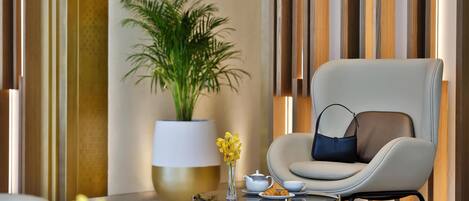 A modern lounge area with a comfortable chair, a glass coffee table, a potted plant, and a vase with yellow flowers.
