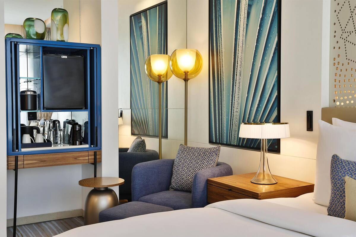 A hotel room with a bed, a seating area, a TV, a coffee machine, and artwork on the walls.