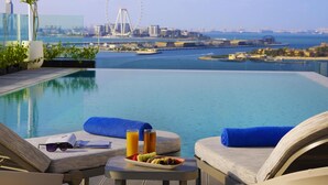 A poolside view with a Ferris wheel in the background, a dining table with food and drinks, and lounge chairs. - Tumbi Hotel Dubai The Palm, Tapestry Collection by Hilton (Dubai)