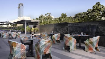 Espace extérieur aménagé avec des chaises et des tables aux motifs originaux, un mur en pierre et une vue sur un grand immeuble en arrière-plan.