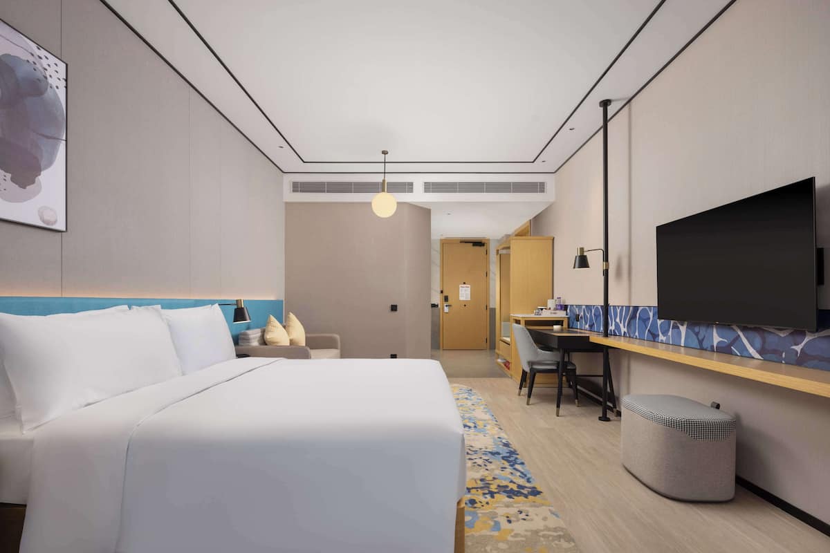 Una habitación de hotel con cama, escritorio, televisión y un cesto de basura.