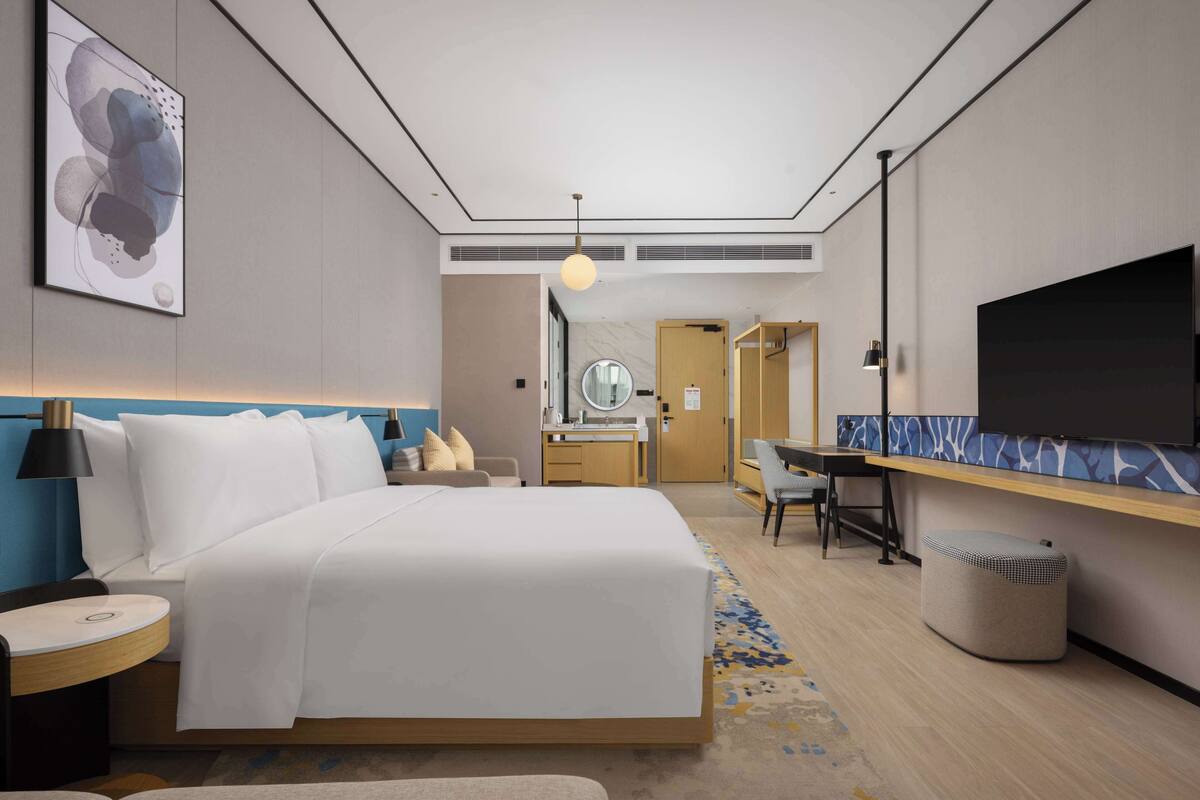 Habitación de hotel con cama, escritorio, una silla, televisión y baño visible al fondo.