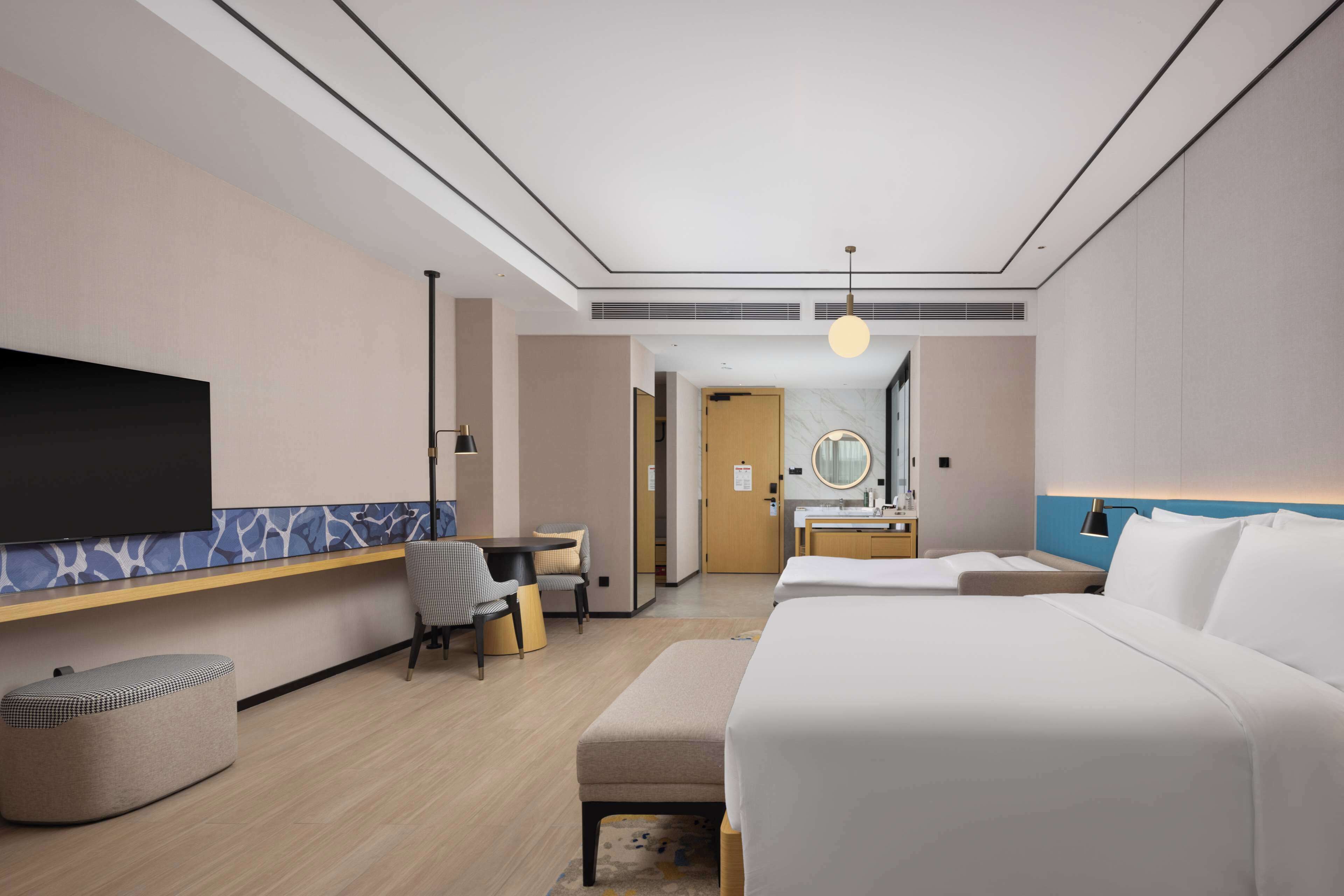Ein Hotelzimmer mit einem großen Bett, einem Schreibtisch mit Stuhl, einem Fernseher, einem Badezimmer mit Spiegel und einer kleinen Sitzecke.