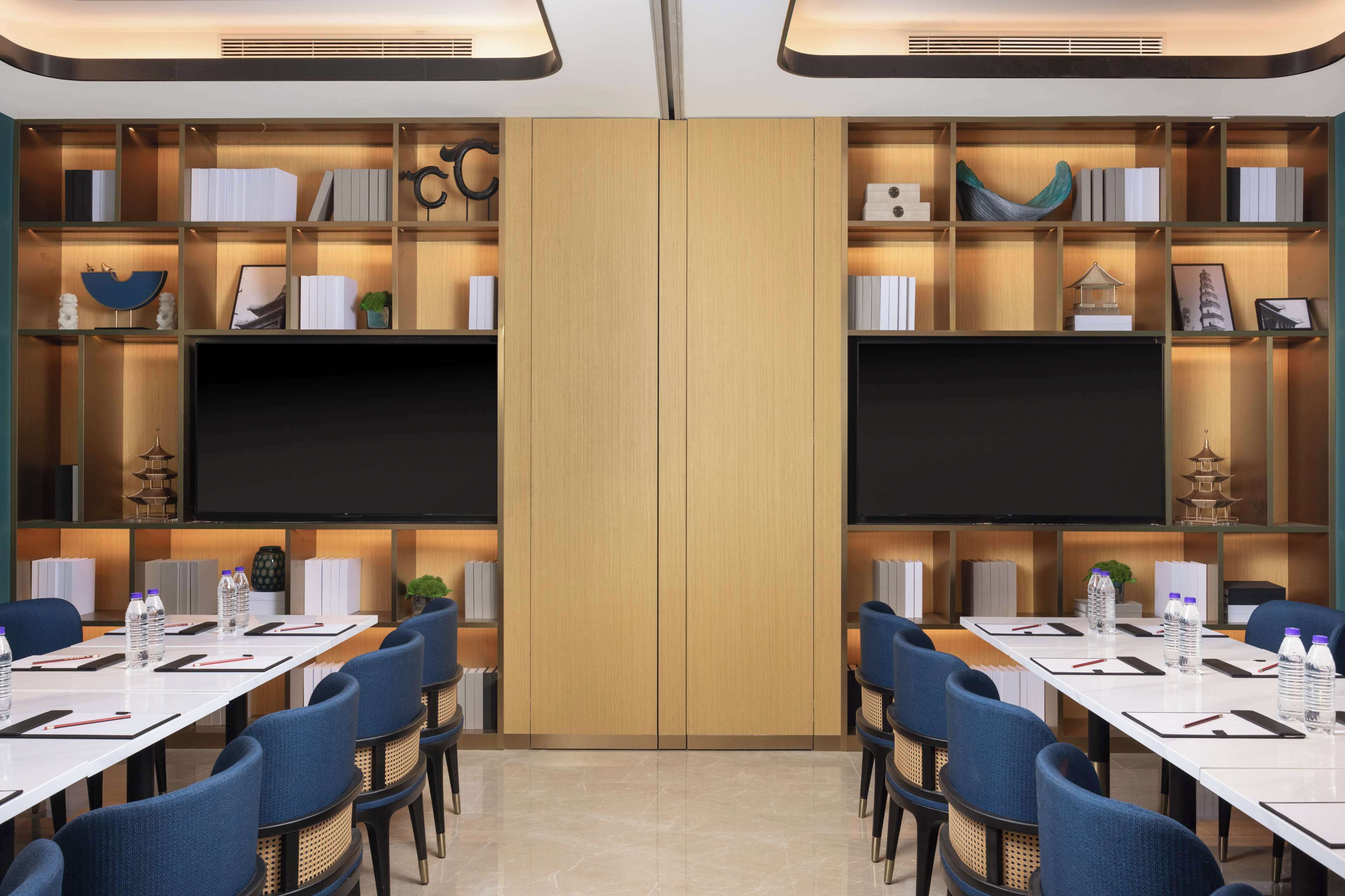 Un salón de conferencias con una gran pizarra, varias mesas con sillas y estanterías con libros y objetos decorativos.