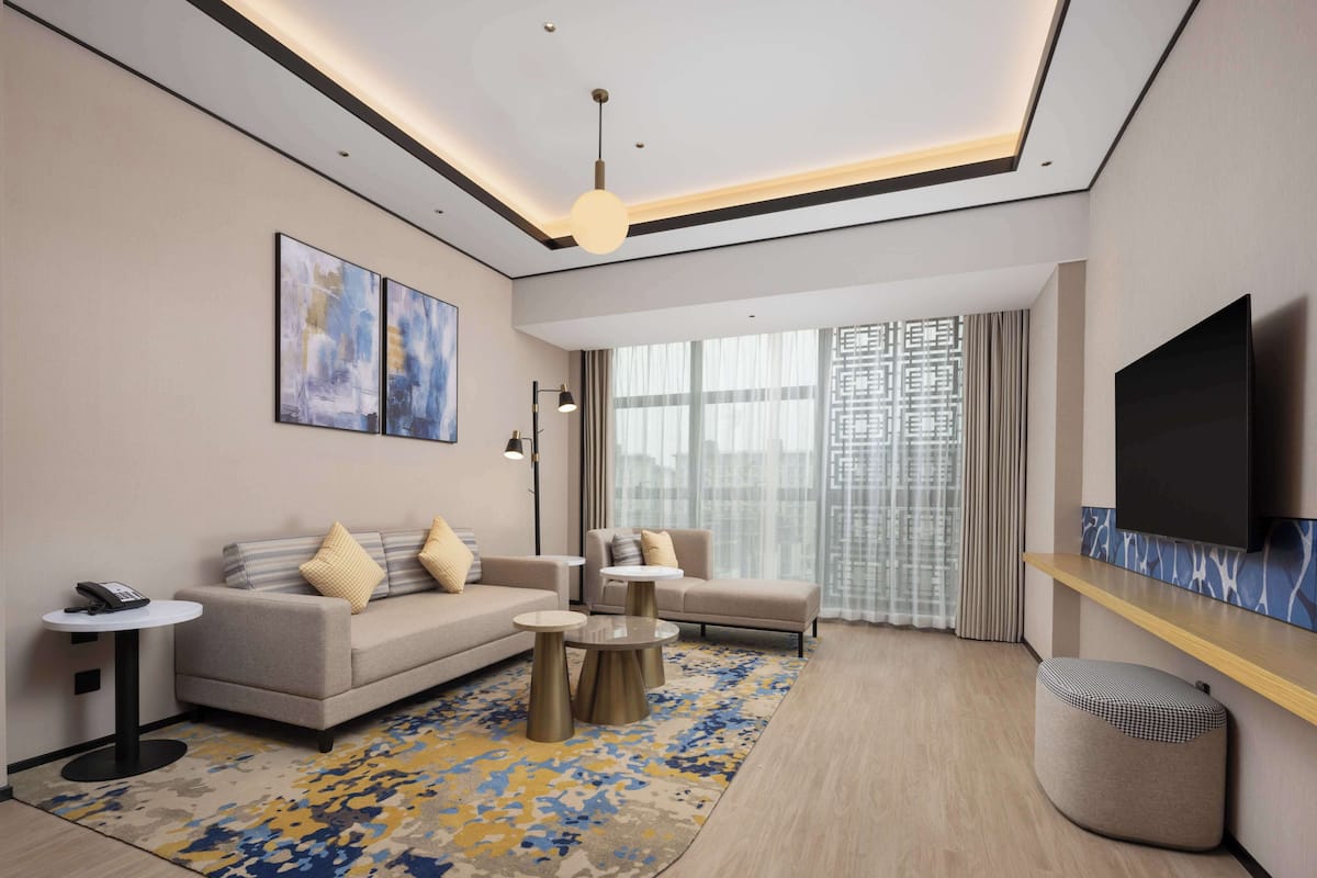 Una habitación de hotel moderna con sofá, sillones, una mesa de centro, televisor y obras de arte en la pared.