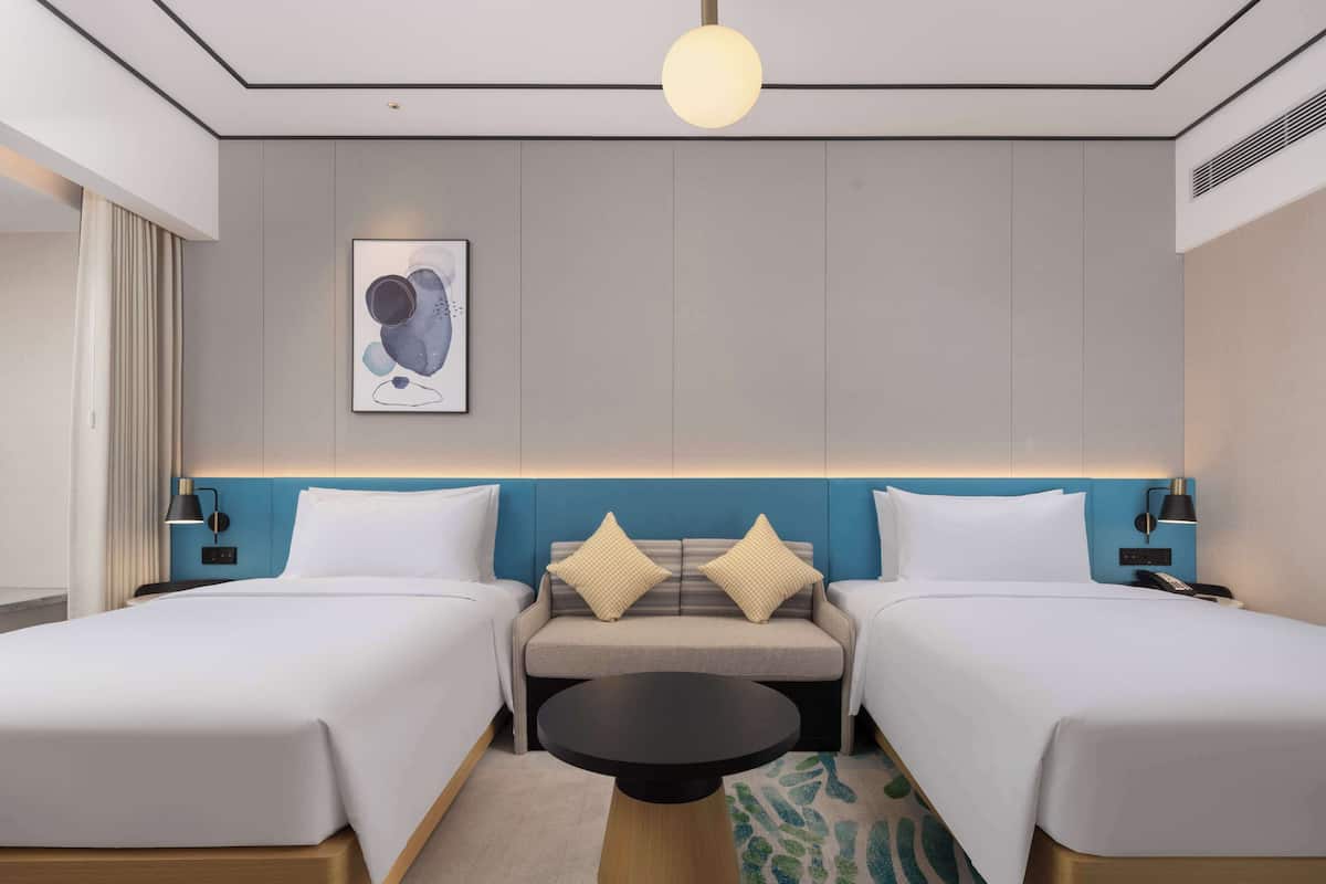 Habitación de hotel con dos camas, un sofá, una mesita y una obra de arte colgada en la pared.