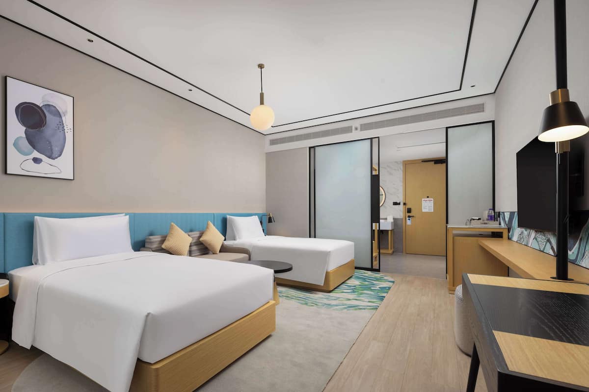 Habitación de hotel con dos camas, un escritorio, una silla, un televisor y un cuadro en la pared.