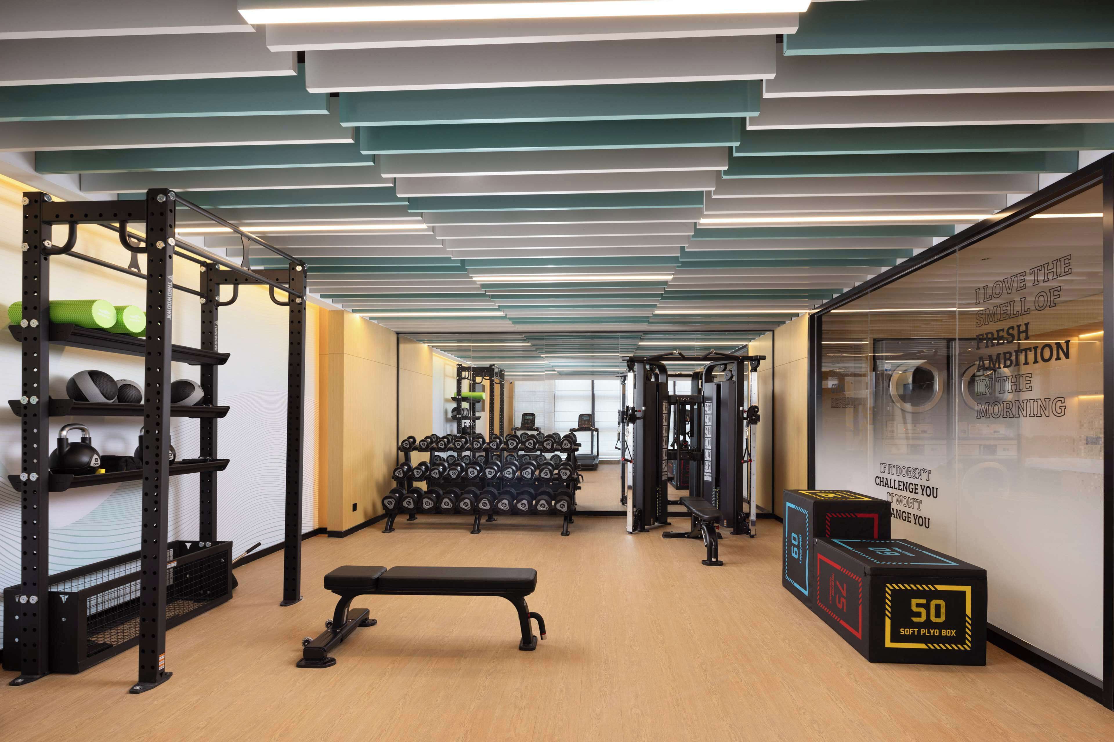 A gym with weight racks, dumbbells, a bench, and a wall with motivational text.