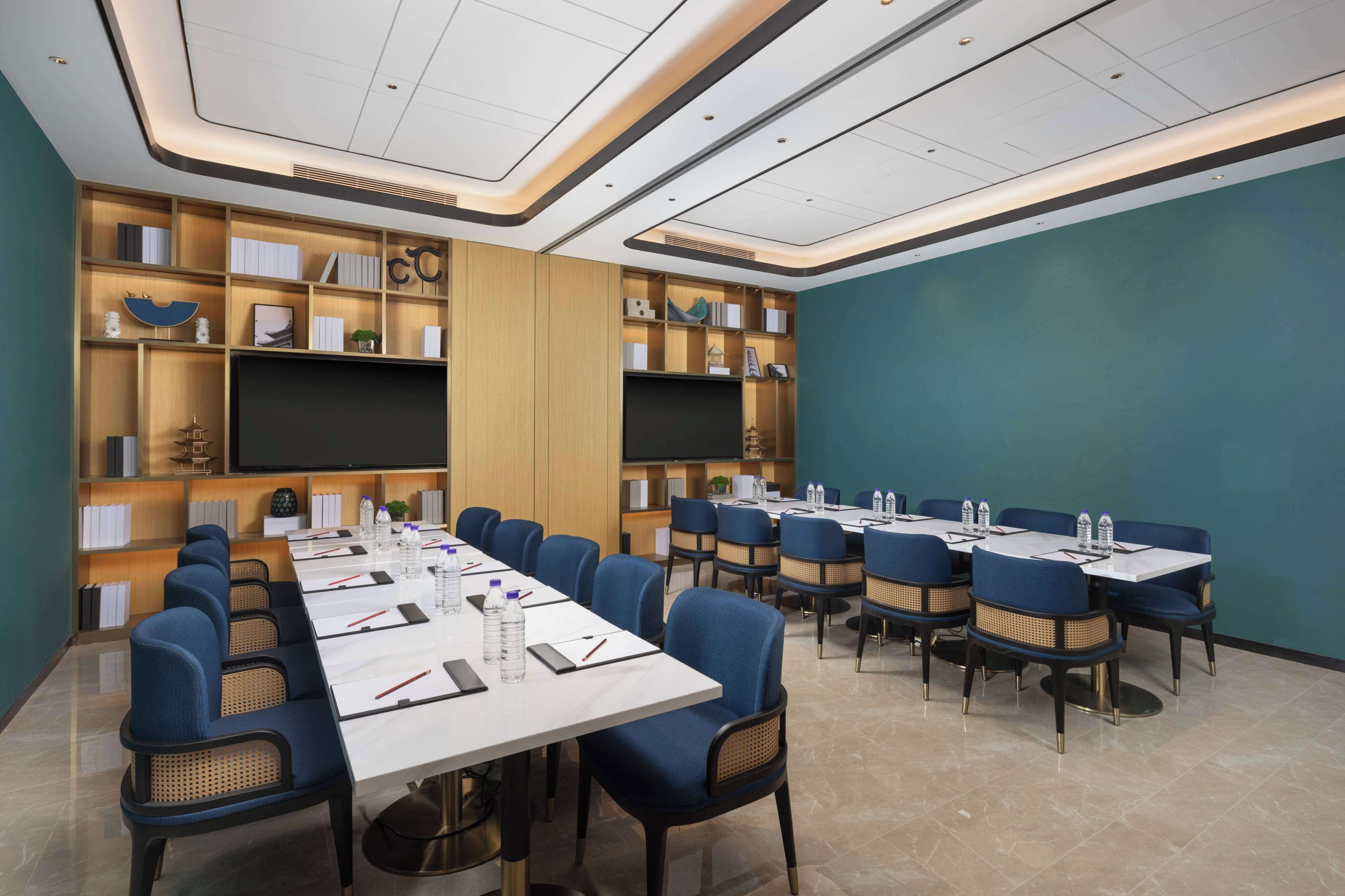 A conference room with a long table, blue chairs, and a large screen.