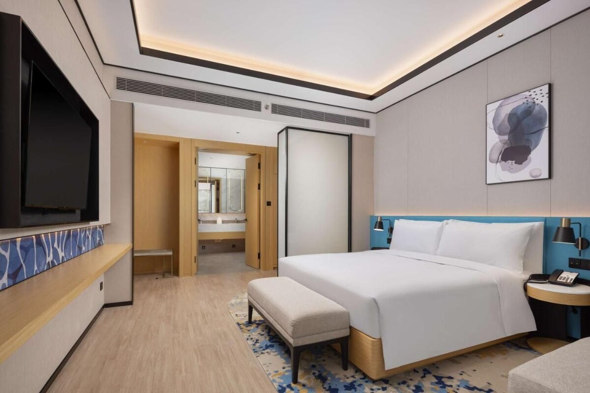 Una habitación de hotel moderna con una cama grande, un televisor, una mesita de noche y un baño visible a través de una puerta abierta.