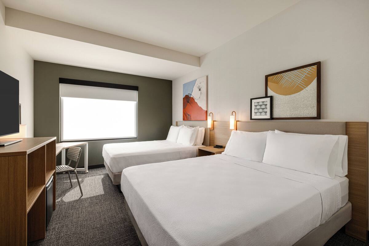 Ein Hotelzimmer mit zwei Betten, einem Schreibtisch, einem Stuhl und Bildern an den Wänden.