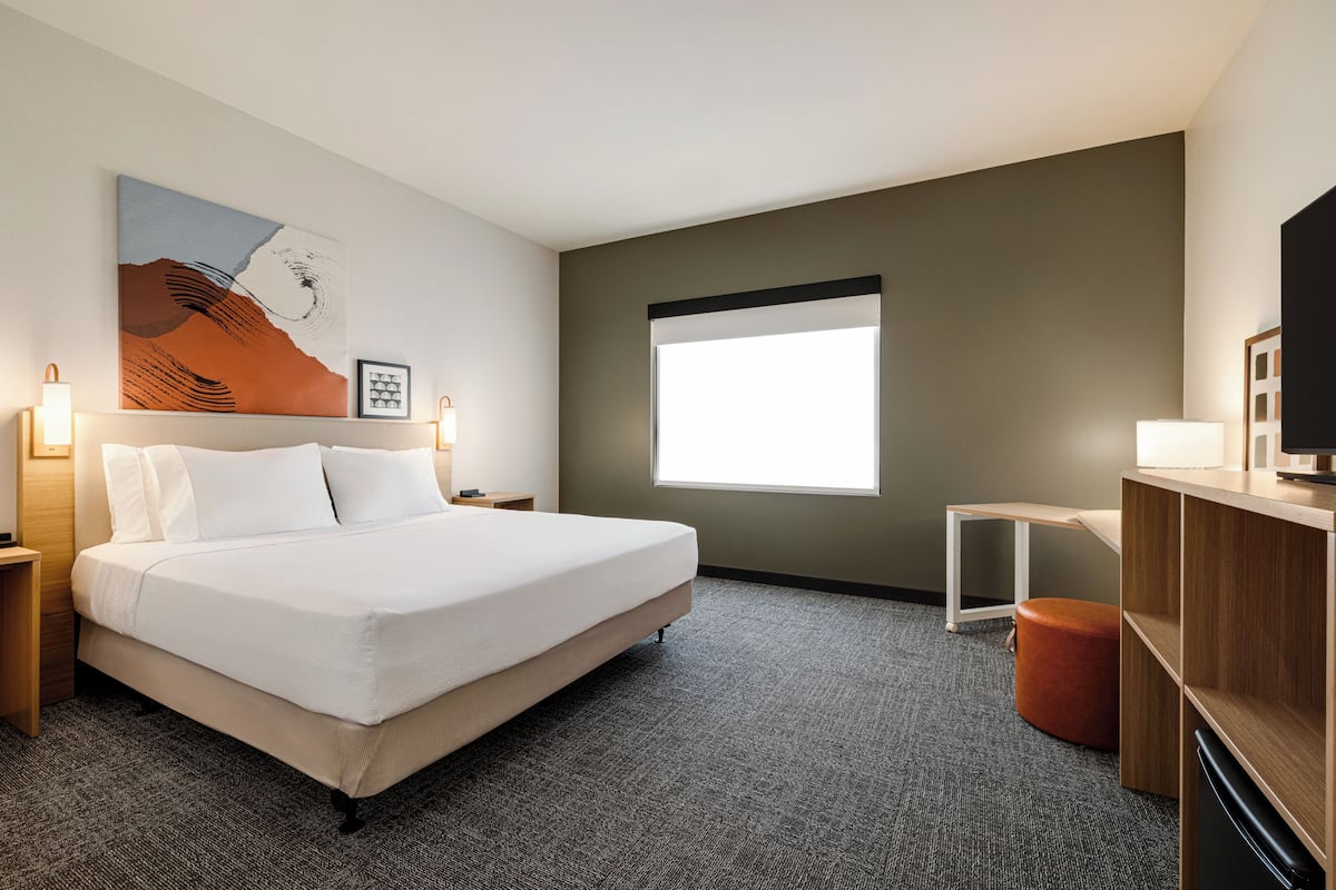Ein Hotelzimmer mit einem großen Bett, einem Schreibtisch, einem Stuhl, einem Fernseher, einem Fenster und Bildern an der Wand.