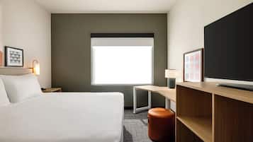 Habitación de hotel con una cama grande, un escritorio, una televisión y una ventana con vistas.