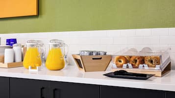 A breakfast buffet setup with orange juice, coffee, and pastries on a white countertop.