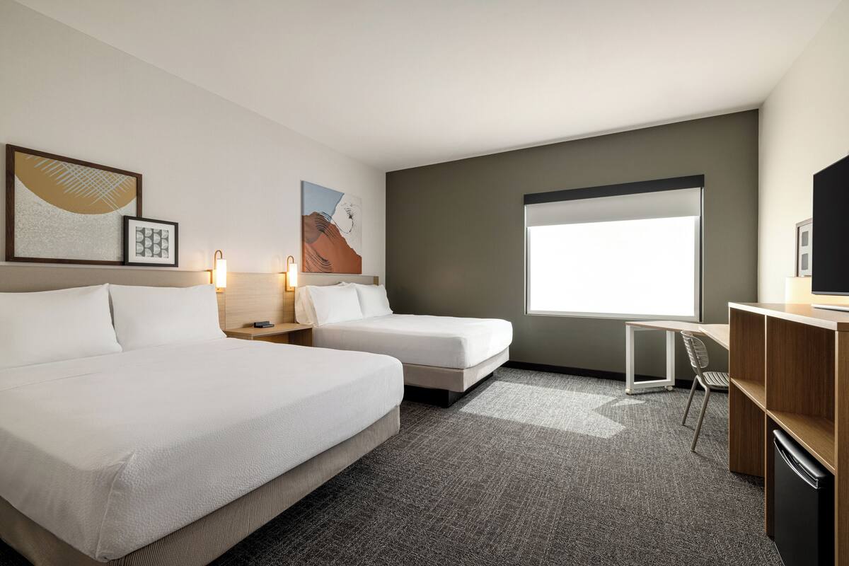 Ein Hotelzimmer mit zwei Betten, einem Schreibtisch, einem Sessel, einem Fernseher und Bildern an den Wänden.