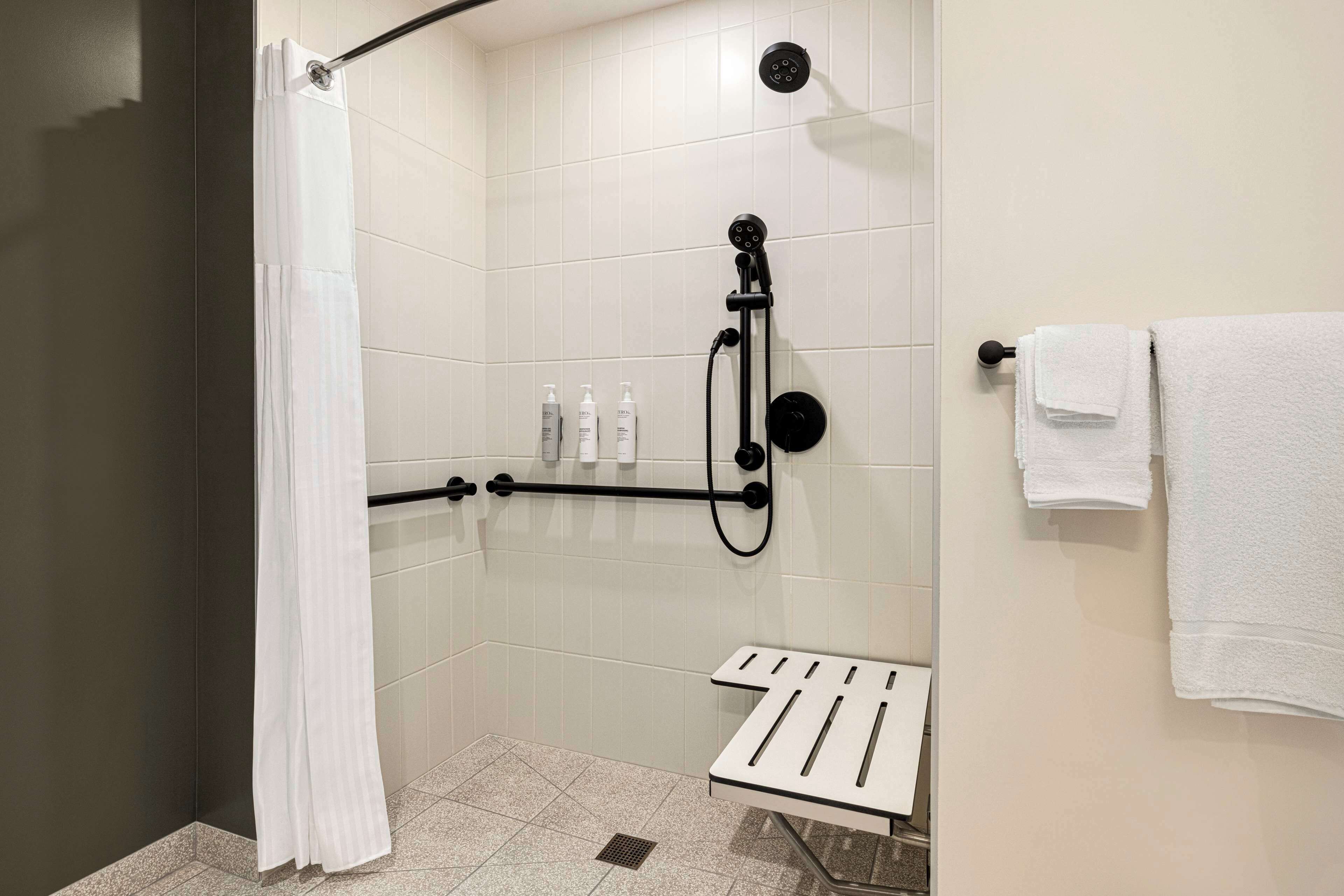 Zona de ducha con puerta de vidrio, ducha de mano y toallero con varias toallas.