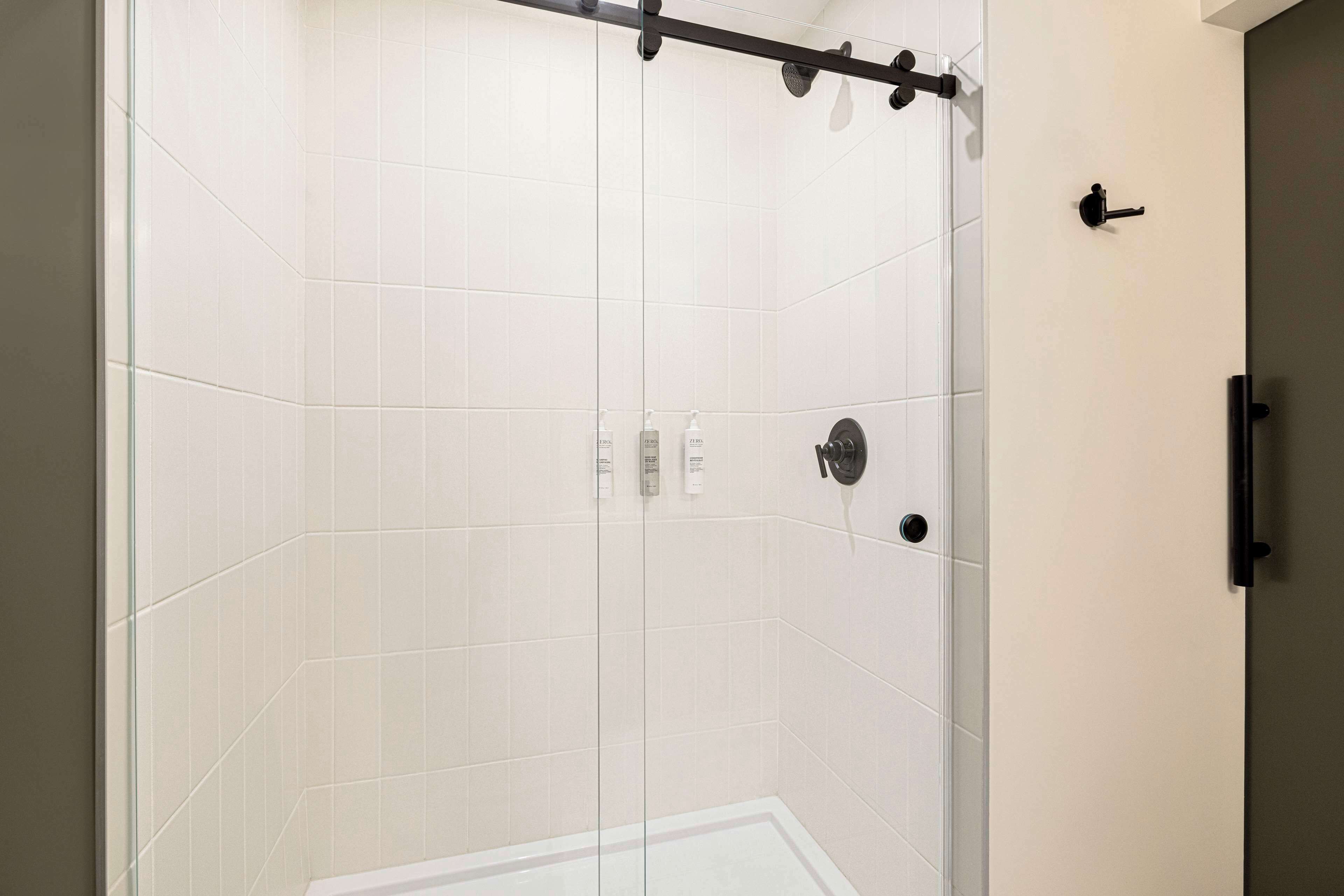 A modern shower area with a glass door, white tiles, and a black towel rack.