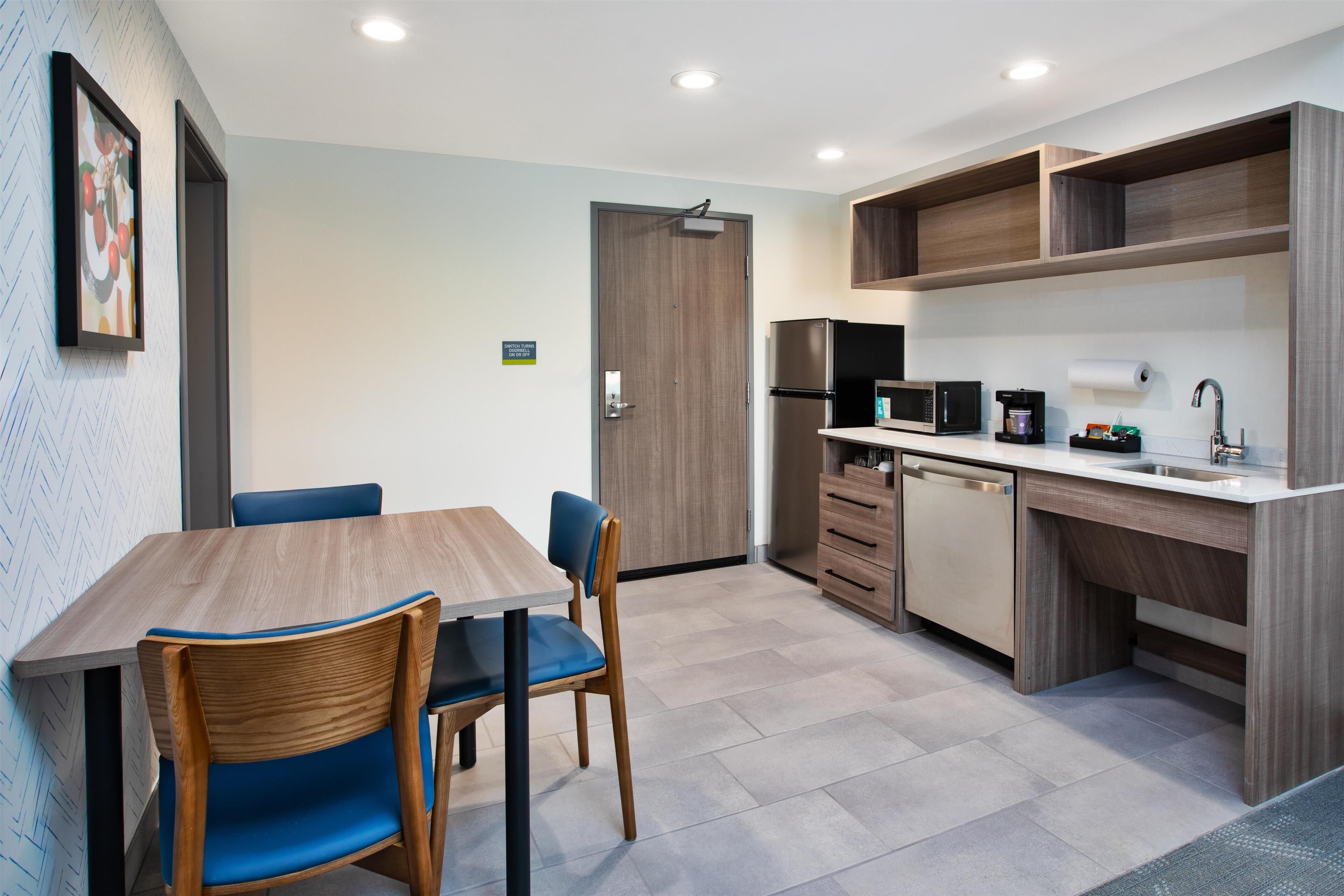 A modern kitchen with a wooden table and chairs, a refrigerator, microwave, and a sink.