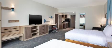 Ein Hotelzimmer mit zwei Betten, einem Schreibtisch, einem Fernseher und einer Küchenzeile.