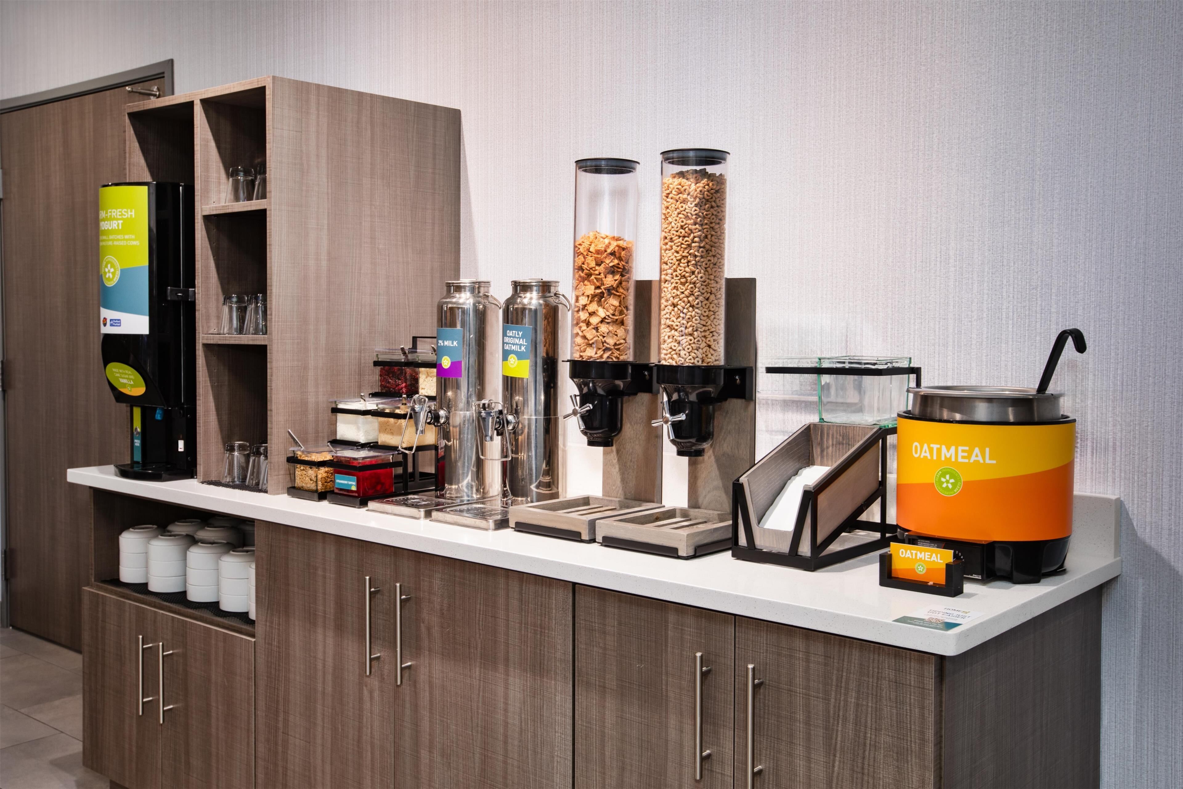 A self-service breakfast station with various food dispensers, including a coffee machine, milk, cereal, and oatmeal.