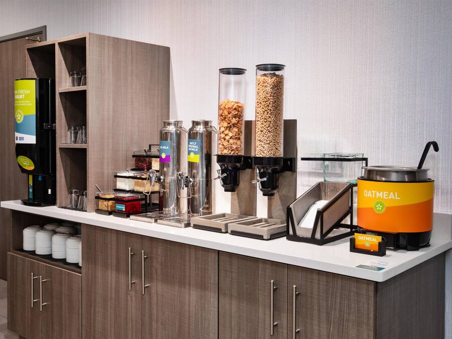 Een ontbijtbuffet met verschillende automaten voor eten, waaronder een koffieapparaat, melk, ontbijtgranen en havermout.
