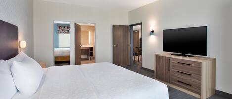 Habitación de hotel con una cama grande, un televisor sobre un mueble de madera y un baño visible a través de una puerta abierta.